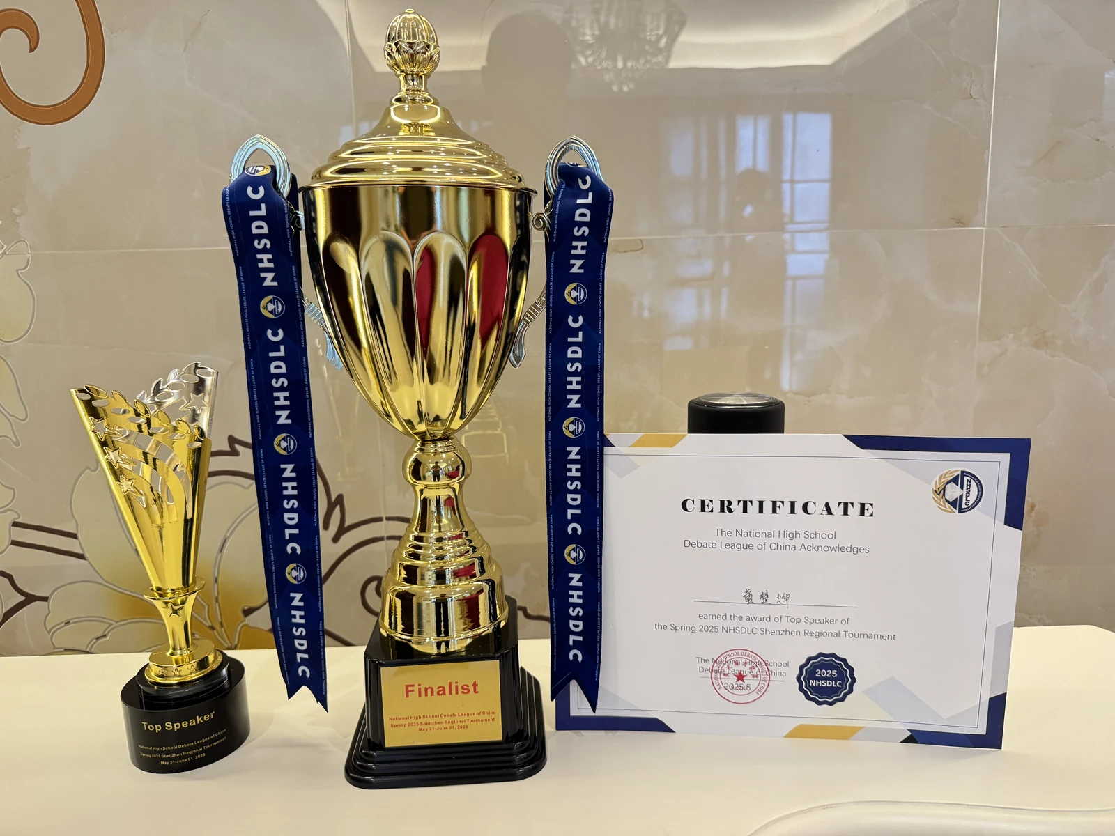 Trophies and a Top Speaker certificate from the 2025 NHSDLC Shenzhen Regional.