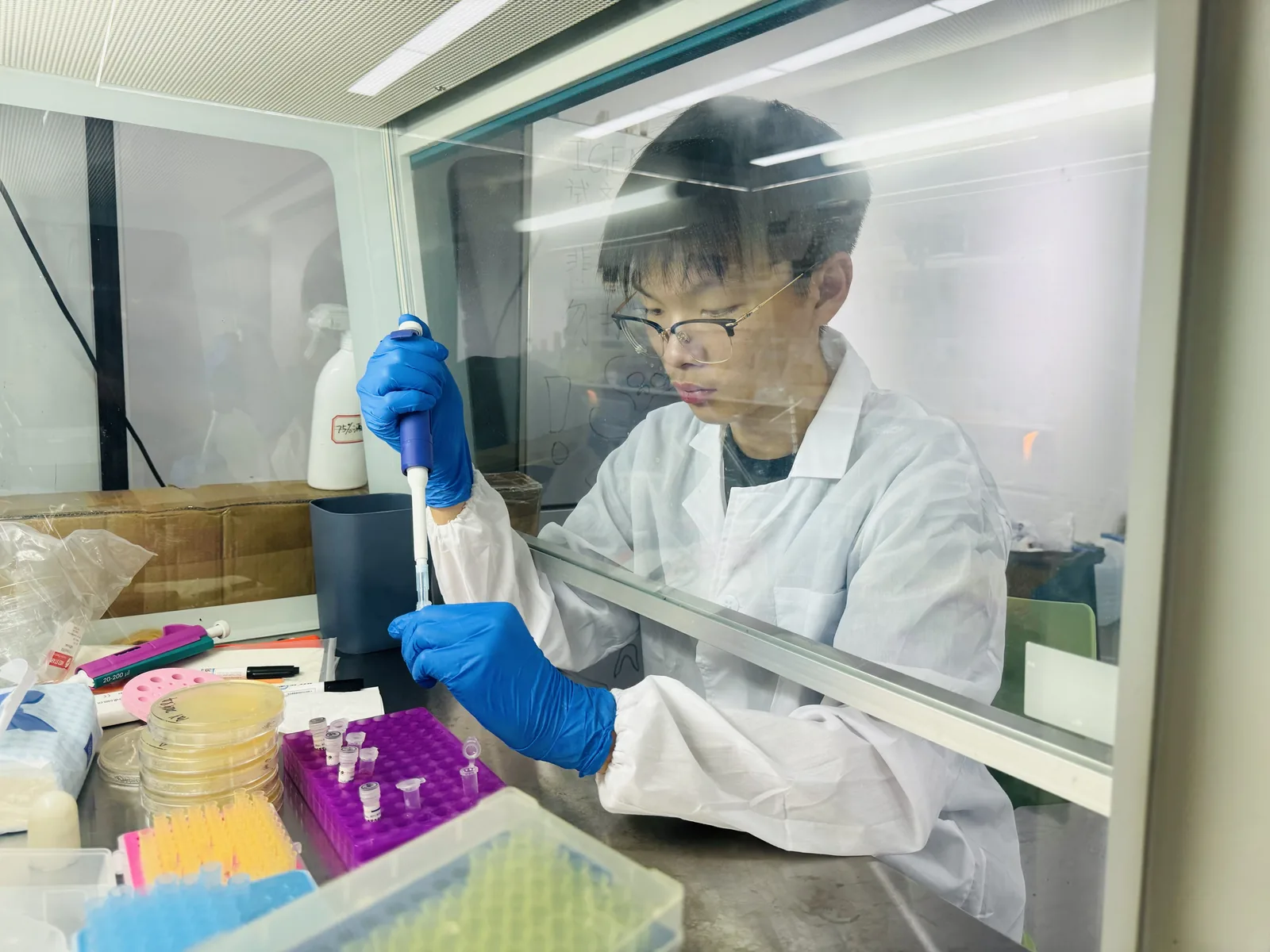 Jacky working at a laboratory bench in a white coat and blue gloves.